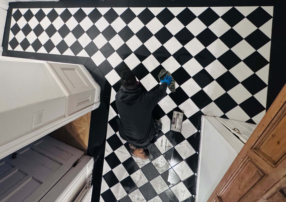Tradesman polishing traditional black and white Victorian checkerboard tiles in a large hallway